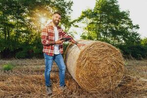 agricultor é em pé ao lado fardos do feno. ele é satisfeito depois de bem sucedido colheita. foto