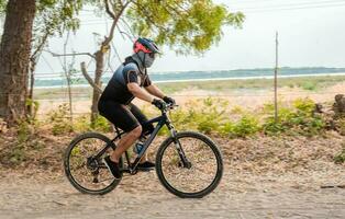 estilo de vida do uma gordo ciclista em a estrada. profissional ciclista em uma sujeira estrada, gordo ciclista em uma sujeira estrada cercado de árvores foto