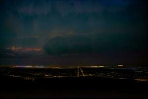 uma Visão do uma cidade às noite a partir de a topo do uma colina. ai gerado foto