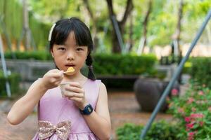 retrato do uma fofa menina comendo a gelo creme copo dentro a parque ao ar livre foto