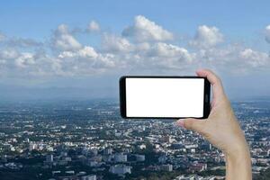 mão segurando Smartphone em branco tela sobre azul céu nuvem e cidade. foto