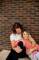 sorridente jovem casal dentro amor dentro frente do casa tijolo parede foto