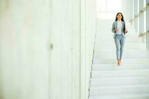 jovem o negócio mulher caminhando baixa a escadas e segurando computador portátil foto