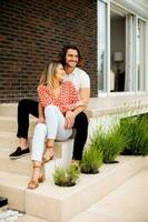 sorridente jovem casal dentro amor sentado dentro frente do casa tijolo parede foto