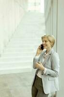 empresária usando telefone celular no corredor do escritório moderno foto