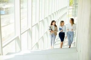 três jovem o negócio mulheres caminhando em escadas dentro a escritório corredor foto