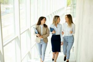 três jovem o negócio mulheres caminhando em escadas dentro a escritório corredor foto