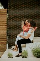 sorridente jovem casal dentro amor sentado dentro frente do casa tijolo parede foto