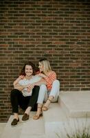 sorridente jovem casal dentro amor sentado dentro frente do casa tijolo parede foto