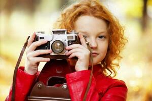 pequeno ruivo menina com uma retro Câmera em a outono fundo. foto