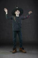 pequeno menina vestindo uma bruxa chapéu em uma Sombrio fundo. foto
