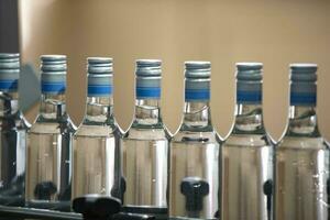 uma grandes linha do vidro garrafas em uma transportador cinto. Produção do alcoólico bebidas. foto