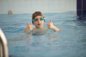 Garoto dentro uma natação boné e natação óculos dentro a piscina. a criança é acionado dentro a natação seção. foto