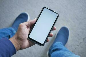 pov tiro do jovem homem mão usando inteligente telefone com branco tela enquanto sentado foto