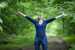 feliz meia idade mulher espalhar dela braços dentro a floresta. foto