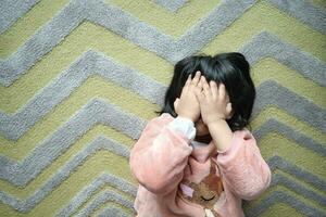 uma chateado criança menina cobrir dela face com mão foto