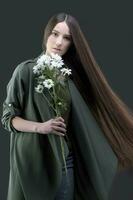 uma lindo jovem menina com natural beleza com grandes suave cabelo detém uma ramalhete do branco crisântemos. foto