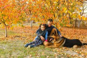 jovem família com uma cachorro dentro folhas em a outonos dia foto