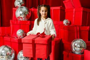 alegre fofa pequeno criança menina com presente. pequeno menina é entre a Natal presentes. foto