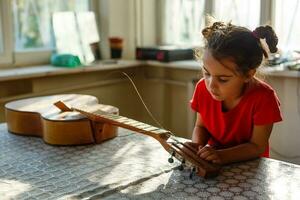 pequeno menina segurando uma quebrado guitarra, guitarra reparar foto