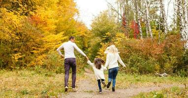 cenário do adorável família dentro outono parque, jovem pais com agradável adorável filha jogando ao ar livre, ter Diversão em quintal dentro cair, feliz família apreciar outonal natureza foto