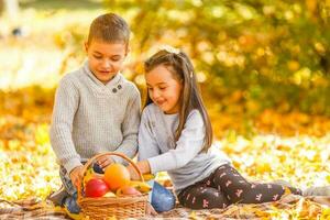 feliz crianças comendo vermelho maçã enquanto caminhando dentro outono parque foto