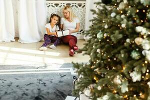 feliz família mãe e criança menina perto uma Natal árvore com Natal presente foto