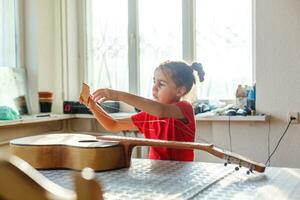 pequeno menina segurando uma quebrado guitarra, guitarra reparar foto