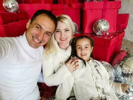 família, feriados, tecnologia e pessoas - sorridente mãe, pai e pequeno menina fazer selfie com Câmera sobre vivo quarto e Natal árvore fundo foto