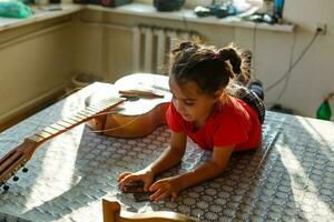 pequeno menina segurando uma quebrado guitarra, guitarra reparar foto