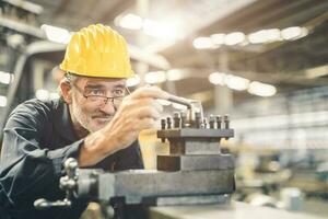 Senior masculino trabalhador engenheiro trabalhando Alto habilidade e precisão com cnc torno máquina metal aço fábrica. saudável idosos trabalhador moagem máquina foto