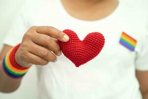 ásia senhora vestindo arco Iris bandeira pulseiras e aguarde coração, símbolo do lgbt orgulho mês comemoro anual dentro Junho social do gay, lésbica, bissexual, transgênero, humano direitos. foto