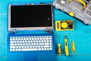 assistente repara laptop com ferramentas e mãos na mesa de madeira azul. vista do topo foto
