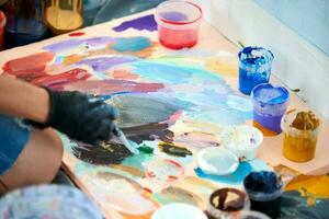 artista mão dentro Preto luvas detém pintura escova e escolher cor a partir de colorida paleta às arte festival foto