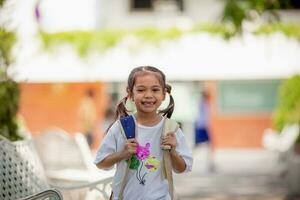 costas para escola. fofa ásia criança menina com uma mochila corrida e indo para escola com Diversão foto