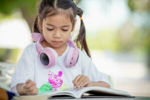 costas para escola. ásia menina lendo uma livro. primário escola alunos depois de Aulas Aprendendo trabalho de casa. foto