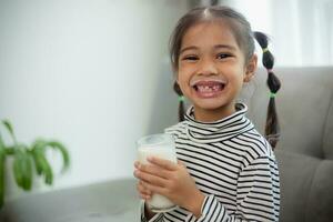 ásia pequeno fofa criança segurando uma copo do leite dentro a casa. sentir feliz e apreciar bebendo leite. foto