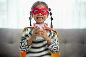ásia pequeno menina dentro uma Super heroi traje bebendo leite às lar. saudável conceito. foto