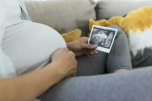 grávida mulher segurando ultrassom imagem. conceito do gravidez, saúde Cuidado, ginecologia, remédio. jovem mãe esperando do a bebê. fechar-se, cópia de espaço, dentro de casa. foto