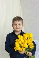 retrato do uma jovem, lindo garoto. detém uma enorme braçada do fresco amarelo tulipas. a conceito do Primavera e feriado, marcha 8, internacional mulheres dia foto