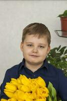 retrato do uma jovem, lindo garoto. detém uma enorme braçada do fresco amarelo tulipas. a conceito do Primavera e feriado, marcha 8, internacional mulheres dia, foto