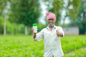 indiano feliz agricultor segurando esvaziar garrafa dentro mãos, feliz agricultor mostrando branco garrafa foto