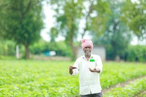 indiano feliz agricultor segurando esvaziar garrafa dentro mãos, feliz agricultor mostrando branco garrafa foto