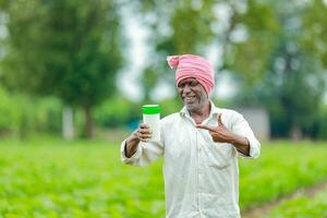 indiano feliz agricultor segurando esvaziar garrafa dentro mãos, feliz agricultor mostrando branco garrafa foto