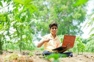 indiano Garoto estudando dentro fazenda, segurando computador portátil dentro mão , pobre indiano crianças foto