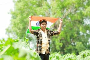 indiano Garoto segurando nacional bandeira dentro fazenda, feliz garoto, nacional bandeira foto