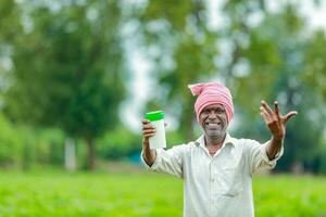 indiano feliz agricultor segurando esvaziar garrafa dentro mãos, feliz agricultor mostrando branco garrafa foto