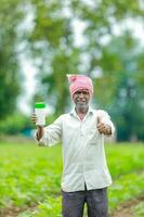 indiano feliz agricultor segurando esvaziar garrafa dentro mãos, feliz agricultor mostrando branco garrafa foto