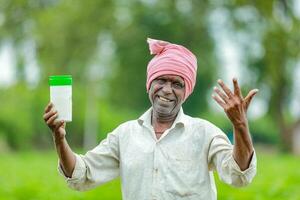 indiano feliz agricultor segurando esvaziar garrafa dentro mãos, feliz agricultor mostrando branco garrafa foto