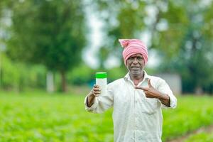 indiano feliz agricultor segurando esvaziar garrafa dentro mãos, feliz agricultor mostrando branco garrafa foto